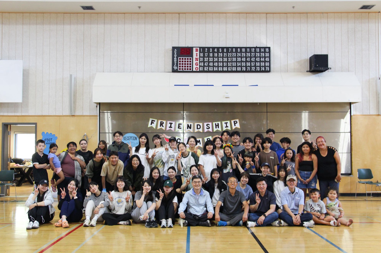 Volunteers and community members pose together under the Friendship Camp banner in the gym