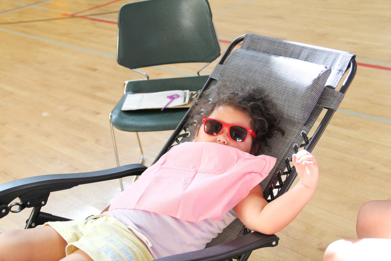 A young girl in red sunglasses relaxes in a reclining chair while waiting for her check-up